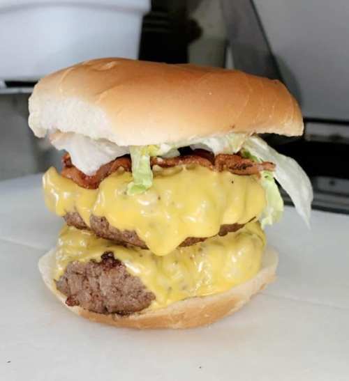 A stacked cheeseburger with two beef patties, melted cheese, lettuce, and bacon, all in a soft bun.