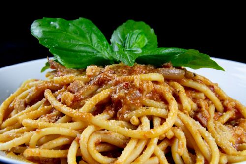 A bowl of spaghetti topped with basil leaves and a rich meat sauce, garnished with grated cheese.