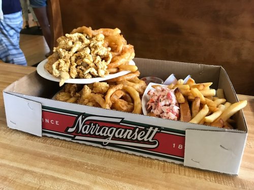 A large box filled with fried seafood, onion rings, fries, and a side of lobster salad.