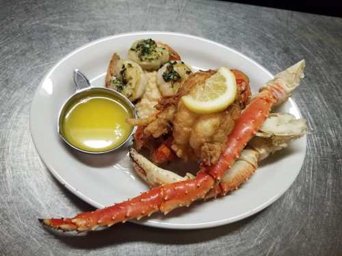 A plate of seafood featuring crab legs, shrimp with garlic butter, and a lemon slice on top.