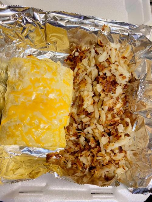 A foil container with a cheesy omelet and crispy hash browns on the side.