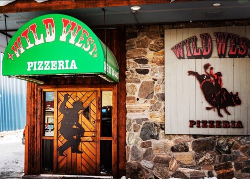 Exterior of Wild Wes Pizzeria featuring a stone wall, green awning, and a wooden door with a silhouette design.