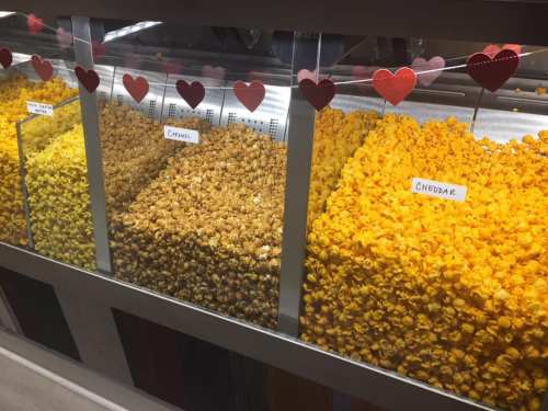 Three bins of popcorn: yellow cheddar, golden caramel, and plain butter, decorated with heart-shaped cutouts.