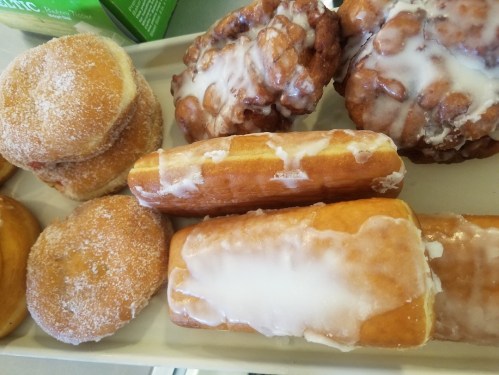 A tray of assorted pastries, including glazed donuts and apple fritters, with a sugary glaze on top.