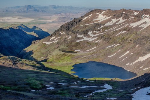 A scenic mountain landscape featuring a tranquil lake surrounded by rugged terrain and distant mountains under a clear sky.