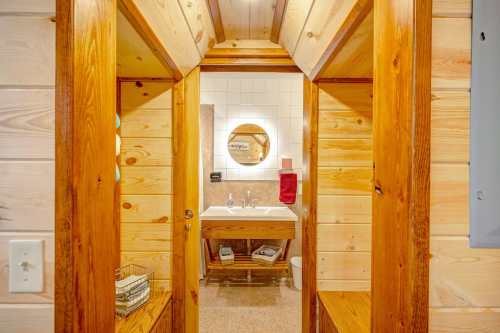 A cozy wooden bathroom with a round mirror, sink, and towel, framed by wooden walls and a warm atmosphere.
