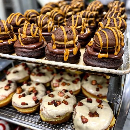 A display of decadent donuts: chocolate and caramel topped, alongside glazed donuts with bacon bits.