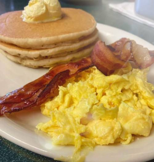 A plate of fluffy pancakes with butter, scrambled eggs, and crispy bacon strips.
