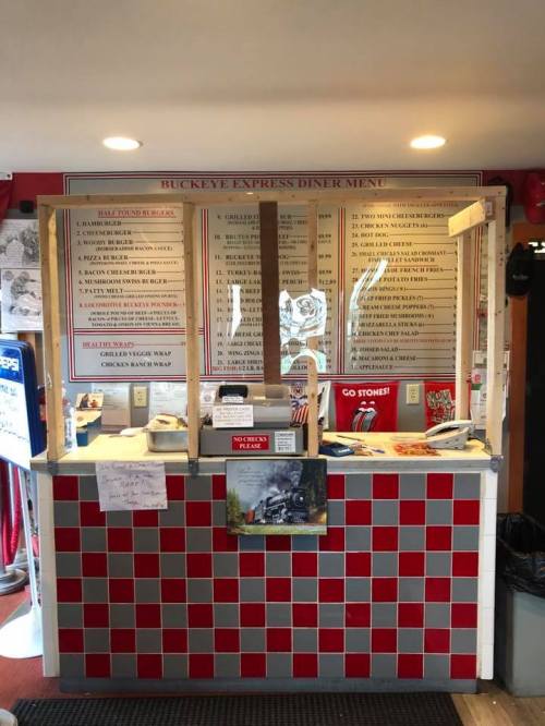 A diner counter with a menu board, red and white checkered design, and food items displayed.