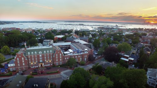 Aerial view of a coastal town at sunset, featuring a hotel, marina, and lush greenery.