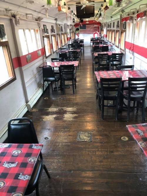 Interior of a dining area with wooden floors, red and white checkered tablecloths, and black chairs in a train car setting.