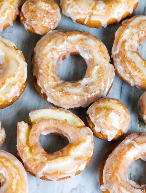 A variety of glazed donuts, including classic rings and a small round donut, arranged on a marble surface.
