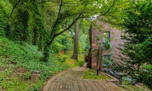 A winding path leads through lush greenery to a brick building nestled among trees.
