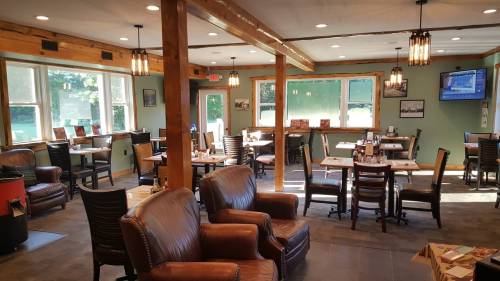 Cozy restaurant interior with wooden beams, leather chairs, and tables, featuring large windows and warm lighting.
