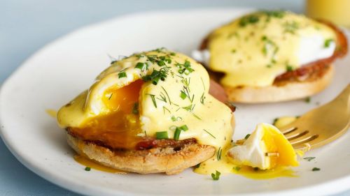 Two eggs Benedict on English muffins, topped with hollandaise sauce and garnished with chives, served on a plate.