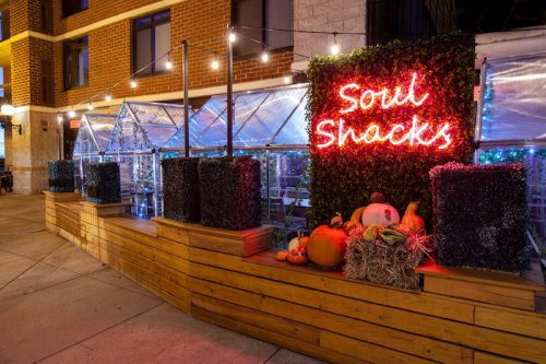 A cozy outdoor dining area with a neon sign reading "Soul Shacks," decorated with pumpkins and string lights.