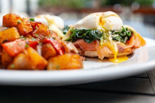 A plate featuring eggs Benedict with spinach and smoked salmon, alongside seasoned roasted potatoes.