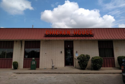 Exterior of a restaurant named "Chicken House," featuring a red roof and sign, with shrubs and a newspaper box outside.