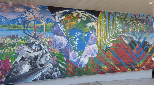 A vibrant mural featuring mountains, flowers, the Earth, crystals, and tropical leaves in a colorful, artistic design.