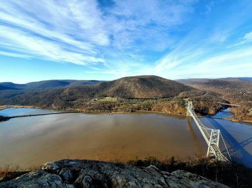 A scenic view of a river and bridge surrounded by rolling hills under a blue sky with wispy clouds.