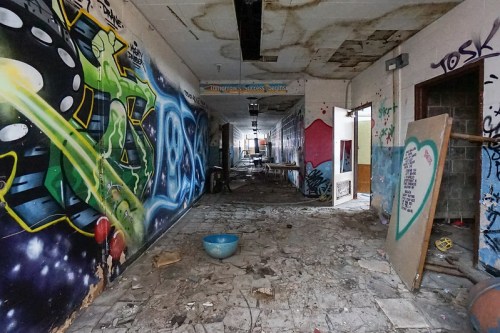 Abandoned hallway with graffiti on walls, debris on the floor, and a blue bowl in the center.
