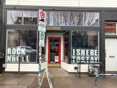 A storefront with large windows displaying the text "ROCK N ROLL IS HERE TO STAY" and a red door.