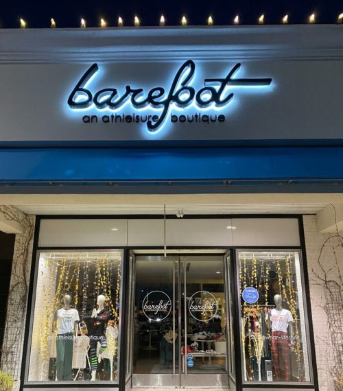 A storefront at night with a sign reading "barebot: an athleisure boutique" and illuminated decorations in the windows.