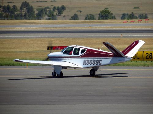 A small, single-engine aircraft with a red and white design taxiing on an airport runway.
