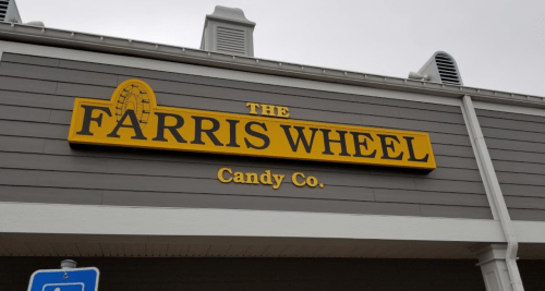 Sign for "The Farris Wheel Candy Co." featuring a yellow and black design on a gray building.