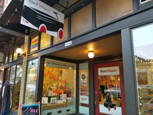 Exterior of Black Wagon store with a sale sign, colorful window displays, and a rainbow flag visible.