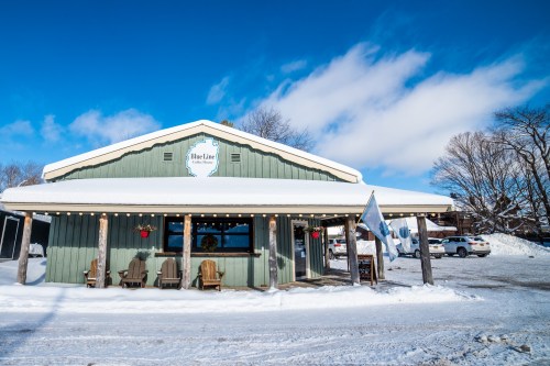 A cozy green building with a sign reading "Blue Line," surrounded by snow and a clear blue sky.
