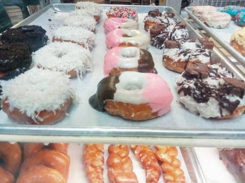 A tray of assorted donuts, including chocolate, pink, and coconut-topped varieties, alongside twisted pastries.
