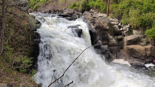 A cascading waterfall flows over rocky terrain, surrounded by lush greenery and trees.