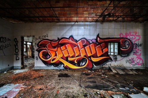 Colorful graffiti on a wall in an abandoned building, with debris scattered on the floor and peeling paint.