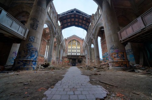 Abandoned church interior with crumbling walls, graffiti, and a broken stained glass window.