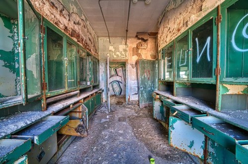 Abandoned room with peeling green cabinets and dusty surfaces, featuring graffiti on the walls.