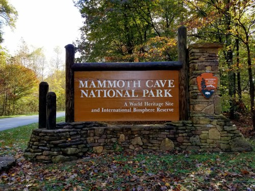 Sign for Mammoth Cave National Park, featuring a wooden structure and colorful autumn foliage in the background.