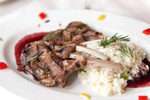 Grilled lamb chops served with creamy risotto and a drizzle of berry sauce, garnished with fresh herbs.