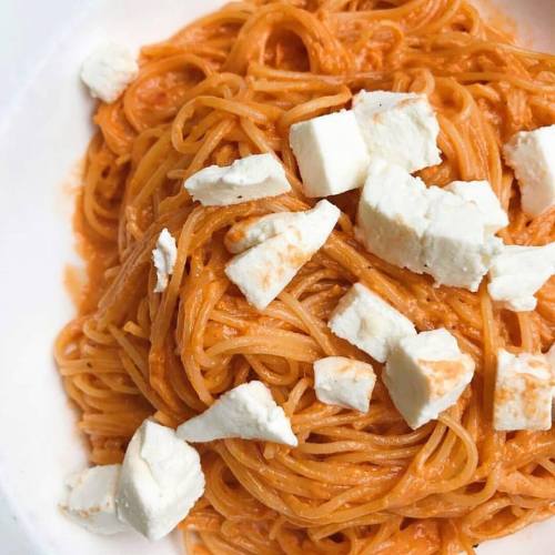 A plate of spaghetti topped with a creamy orange sauce and chunks of white cheese.