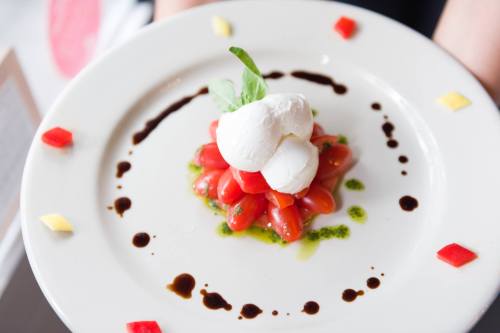 A plate of fresh tomatoes topped with burrata cheese, drizzled with balsamic and pesto, garnished with colorful accents.