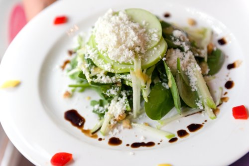 A fresh salad with green apple slices, leafy greens, cheese, and a drizzle of balsamic reduction on a white plate.