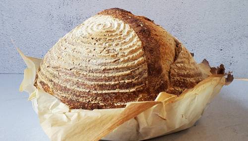 A round, crusty loaf of bread with a spiral pattern on top, resting on parchment paper against a gray background.
