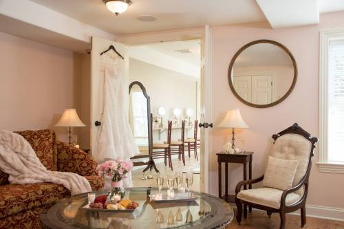 A cozy room with a wedding dress hanging, a mirror, elegant furniture, and a table with flowers and champagne glasses.