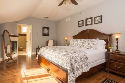 Cozy bedroom with a wooden bed, decorative bedding, and a mirror, featuring warm lighting and a bathroom doorway.