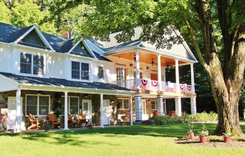 A charming two-story house with a porch, surrounded by greenery and decorated with red, white, and blue bunting.