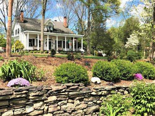 A charming white house with a porch, surrounded by lush greenery and colorful flowers, set against a clear blue sky.