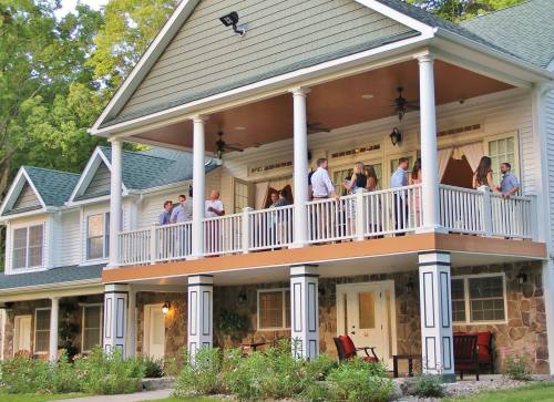 A large house with a spacious porch, where several people are gathered, enjoying the outdoors and socializing.