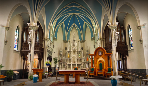 Interior of a church featuring tall arches, stained glass windows, an altar, and ornate wooden furnishings.