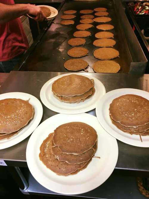 A griddle with multiple pancakes cooking, alongside several plates stacked with pancakes.