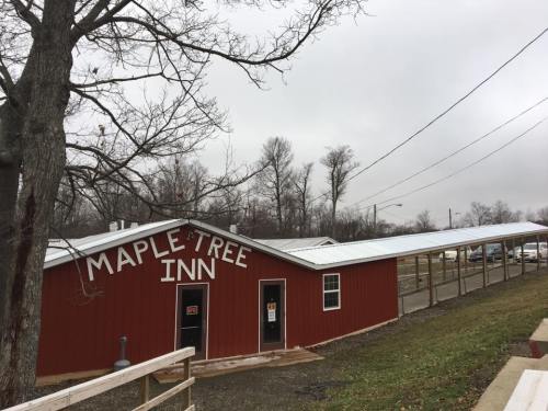 Red building with "Maple Tree Inn" sign, surrounded by bare trees and a cloudy sky. Parking area visible in the background.